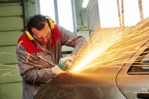 a mechanic working on a severely dented vehicle with a specialized tool, dent repair