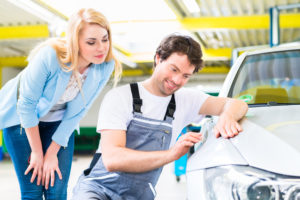 A mechanic doing a dent fix on a car as a female watches from behind