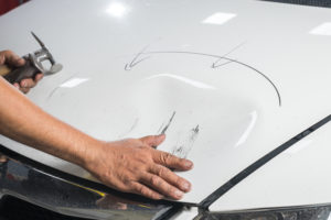 hand on the dented hood of a car, preparing to fix it. 