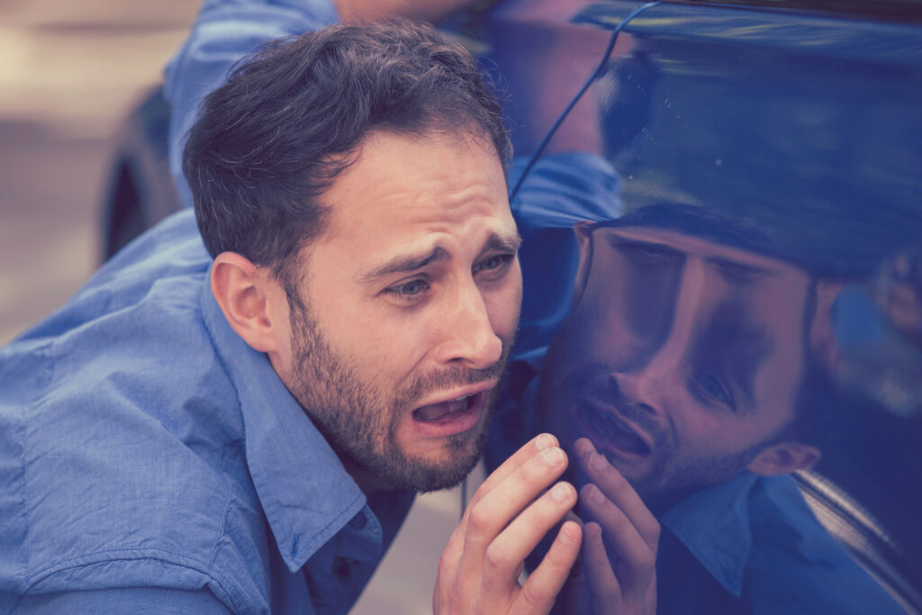 Frustrated upset young man looking at scratches and dents on his car outdoors