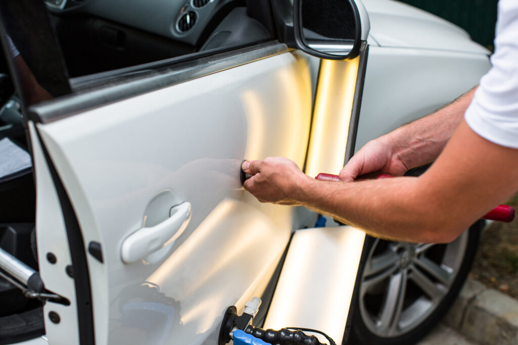 A dent removal specialist tending to a white car’s passenger side door.