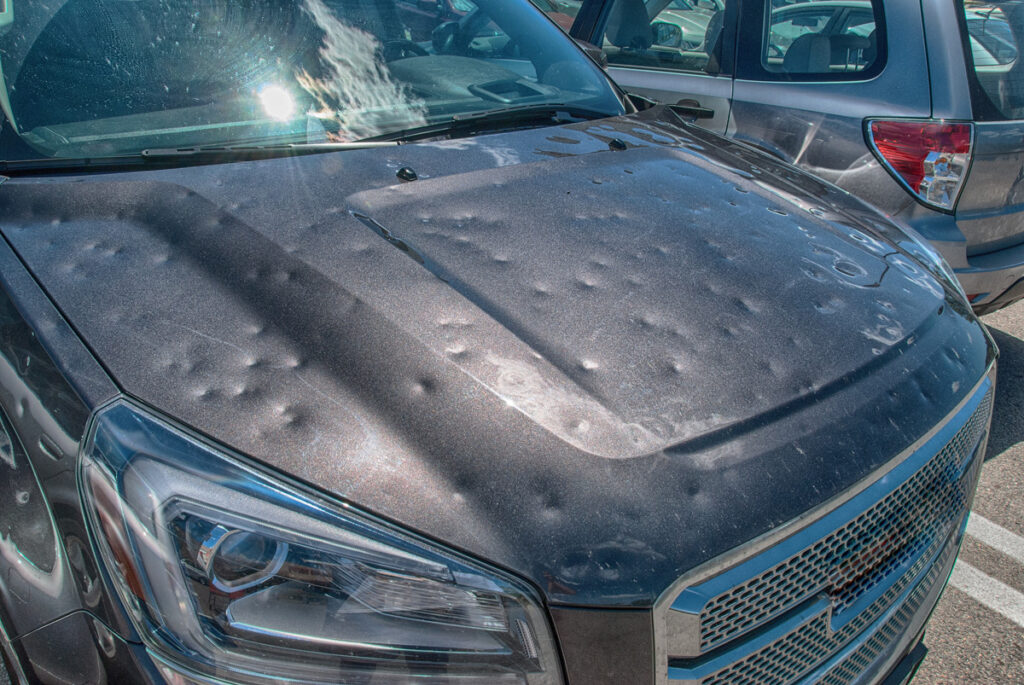 The hood of a grey vehicle with multiple small dents from hail in El Paso.