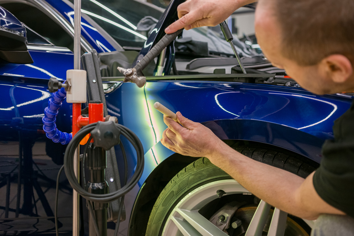 A professional removing a dent from a blue car in El Paso.